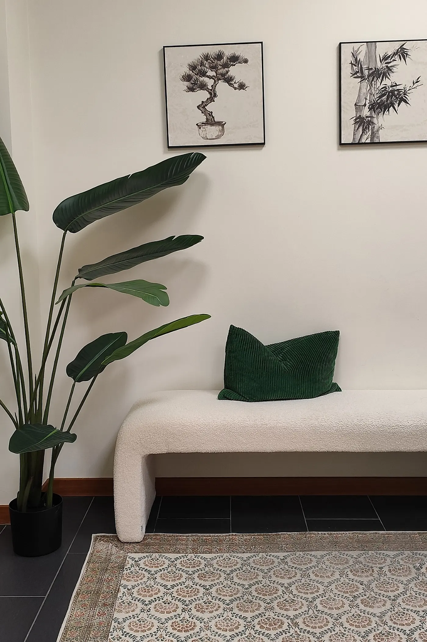 Banco tapizado junto a una planta y dos láminas enmarcadas